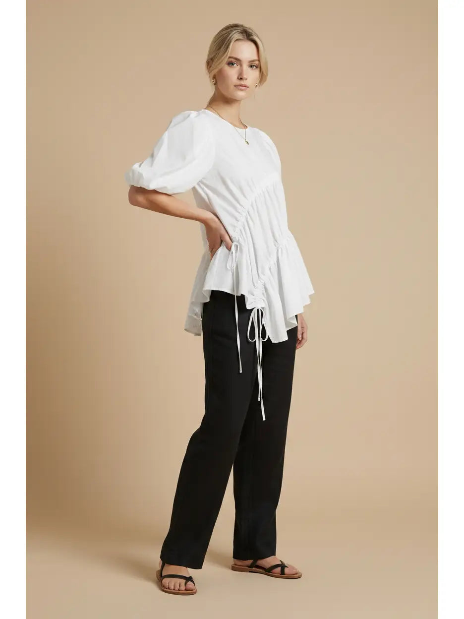 Woman wearing a white blouse and black pants on a beige background