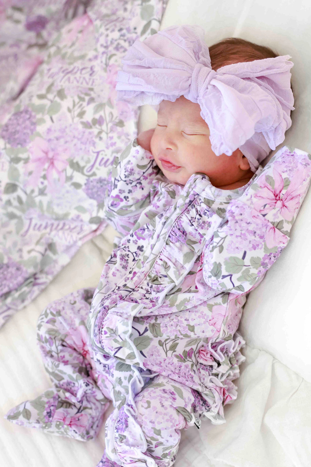 Newborn baby wrapped in a floral outfit with a matching headband on a soft surface.