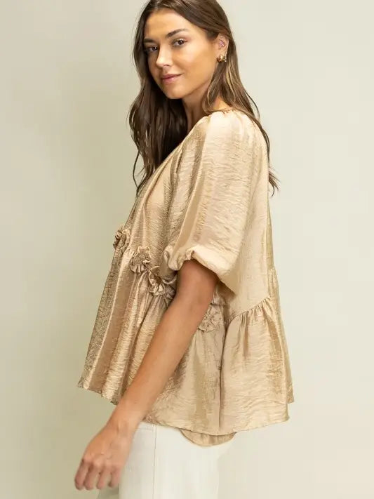 Woman wearing a beige blouse with ruffled sleeves against a plain background