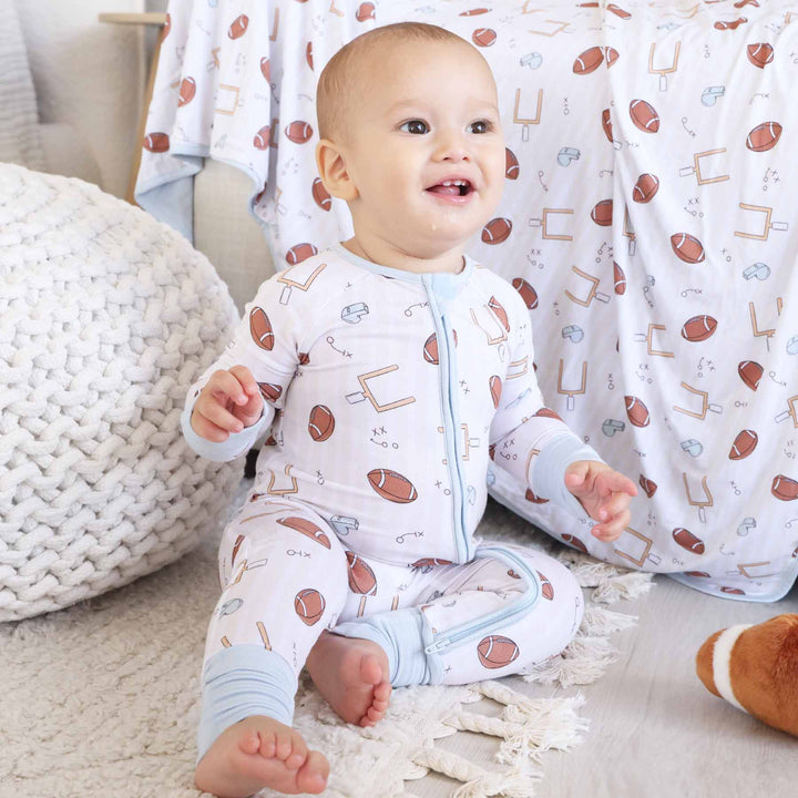 Baby in a onesie with sports-themed print sitting on a carpeted floor.