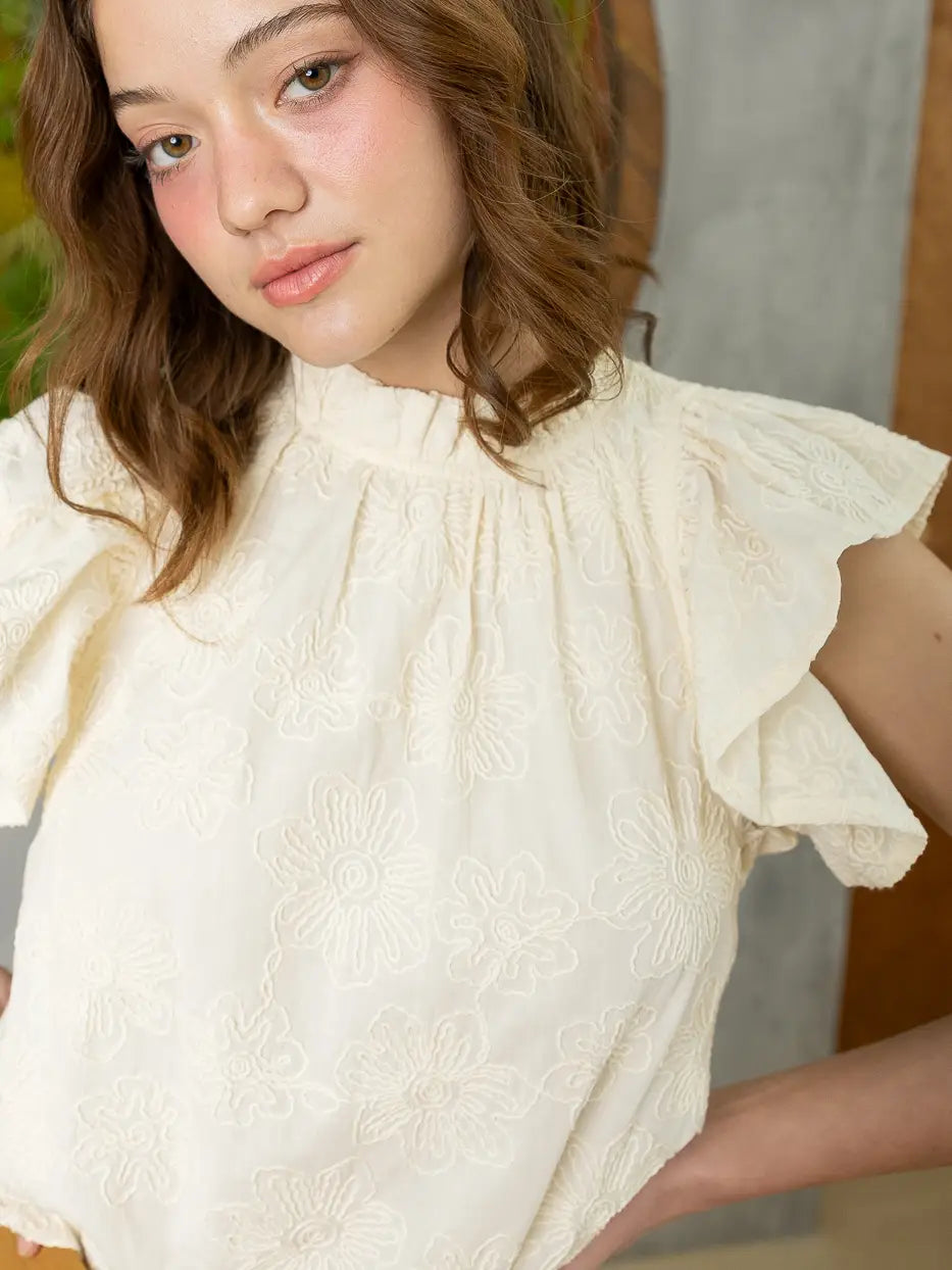 Woman wearing a white blouse with ruffled sleeves against a neutral background