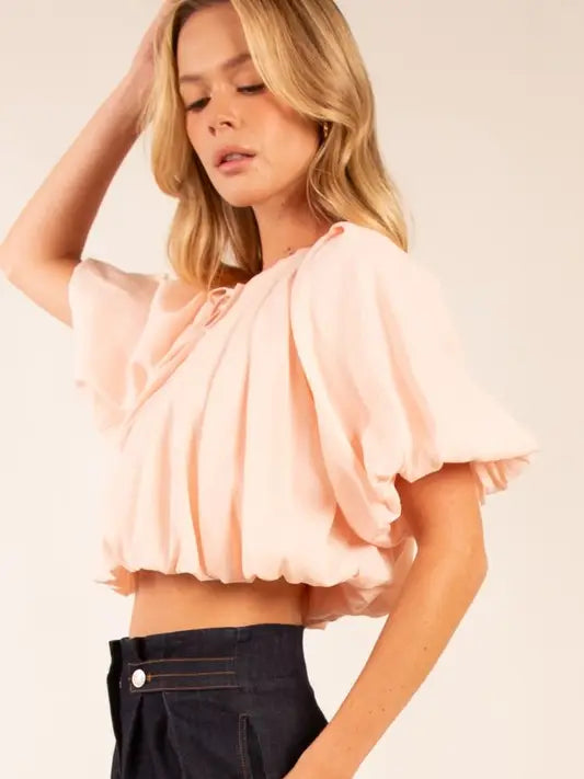 Woman wearing a light pink blouse with ruffled sleeves on a plain background