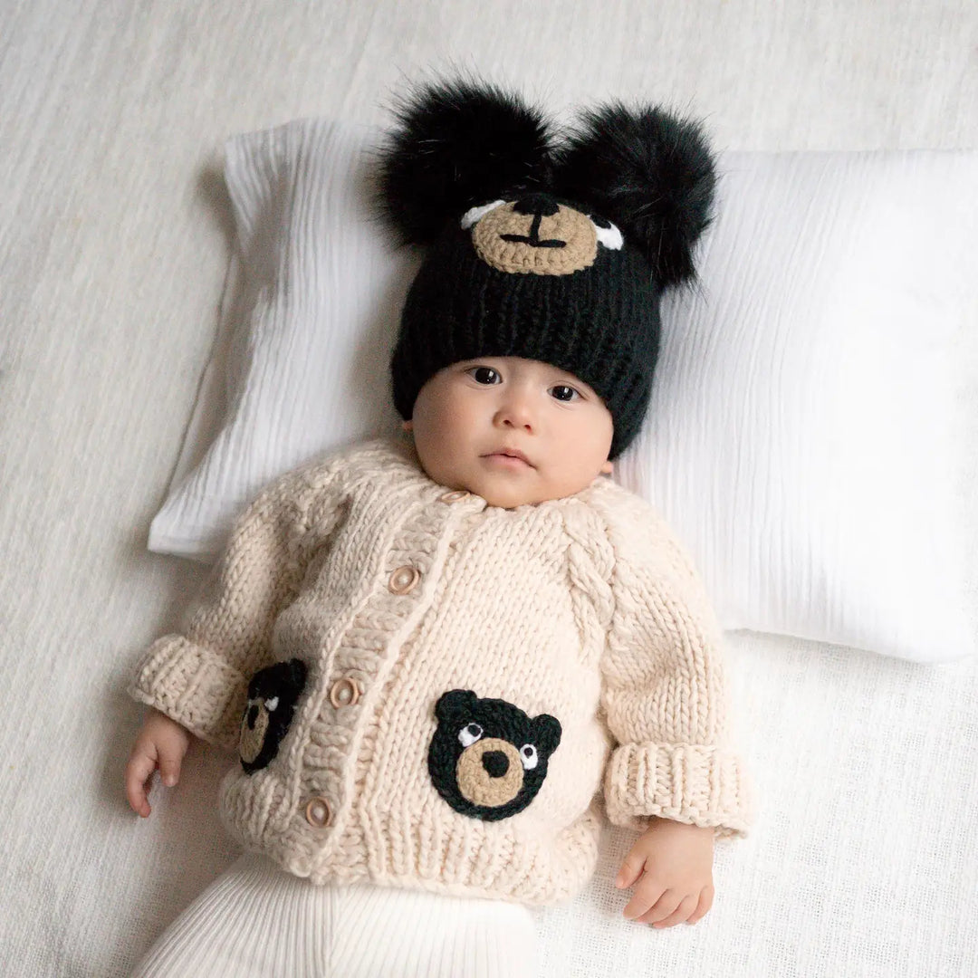 Baby lying on a pillow in the oatmeal Beary Good Friends Baby Cardigan with black bear pockets