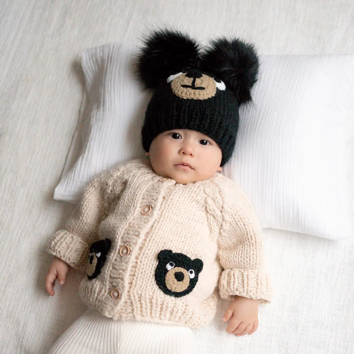 Baby lying on a pillow in the oatmeal Beary Good Friends Baby Cardigan with black bear pockets