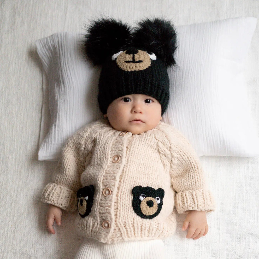 Baby wearing the Beary Good Friends Baby Cardigan with black bear-face pockets and a black bear hat
