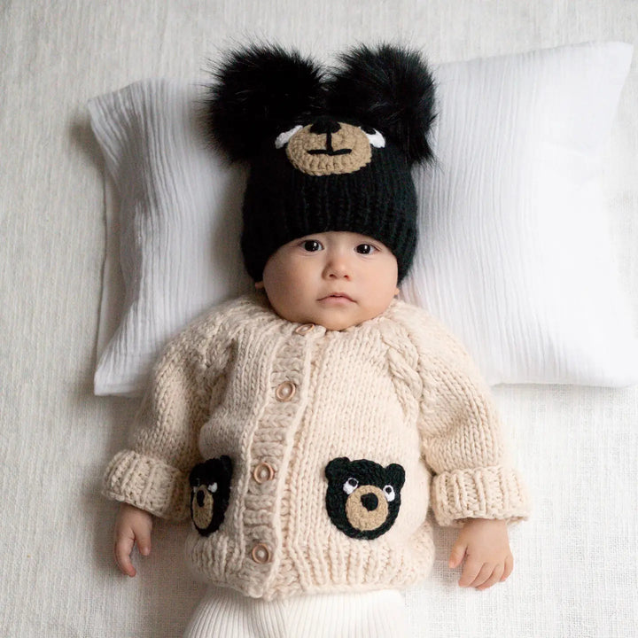 Baby wearing the Beary Good Friends Baby Cardigan with black bear-face pockets and a black bear hat