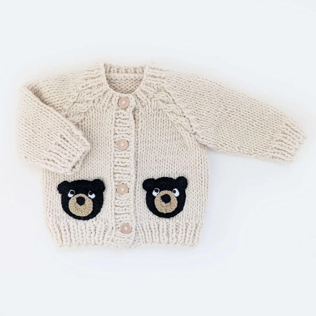Oatmeal hand-knit Beary Good Friends Baby Cardigan with black bear-face pockets on a white background