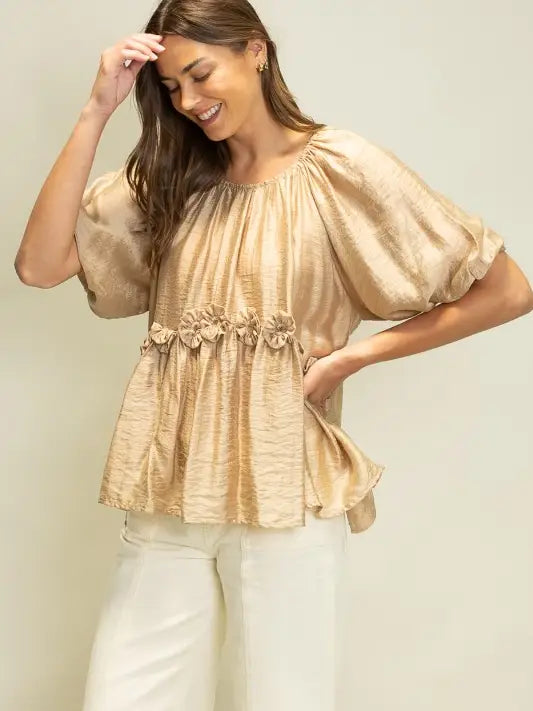 Woman wearing a beige blouse with floral details against a plain background