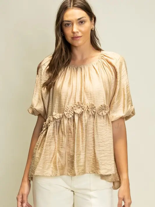 Woman wearing a beige blouse with floral details on a plain background