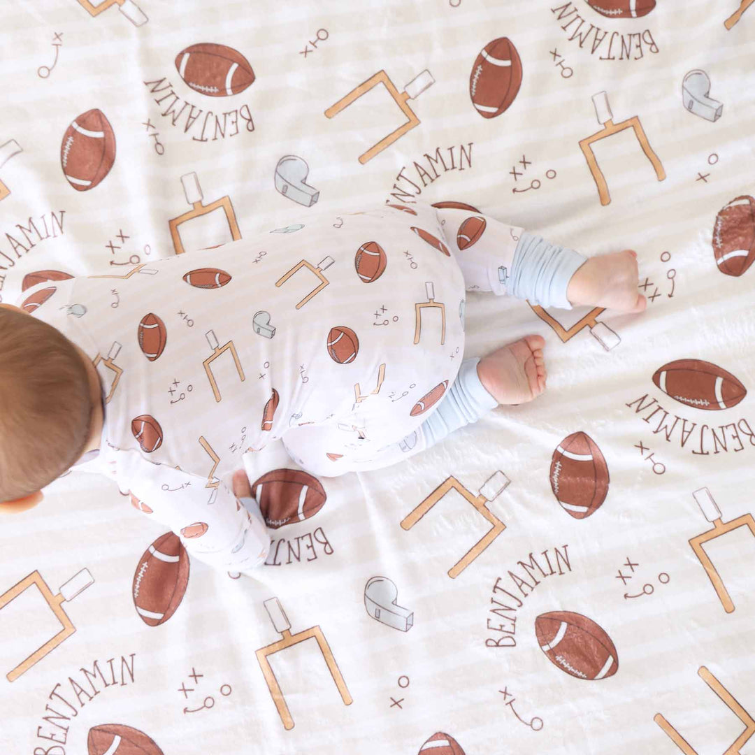 Baby lying on a blanket with football and sports pattern