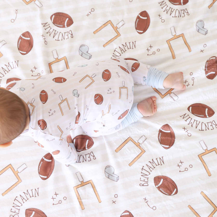 Baby lying on a blanket with football and sports pattern