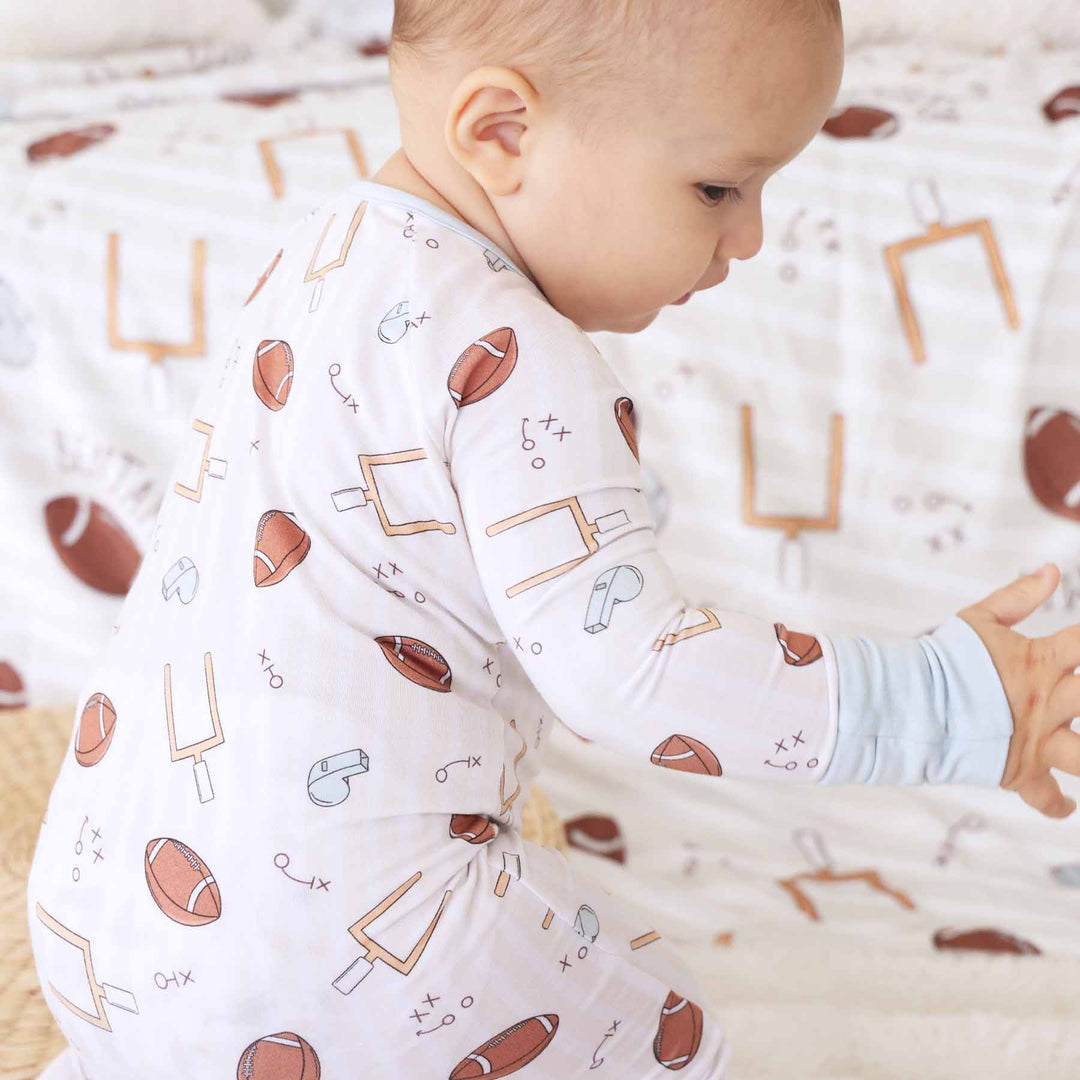 Baby wearing a long-sleeve shirt with sports-themed pattern on a soft, patterned background
