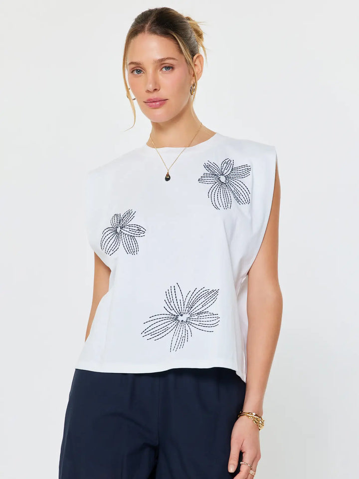 Woman wearing a white sleeveless top with black floral patterns on a plain background
