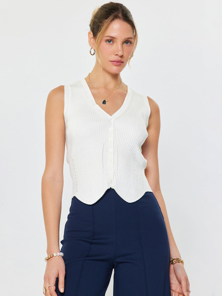 Woman wearing a white sleeveless top and navy pants on a plain background