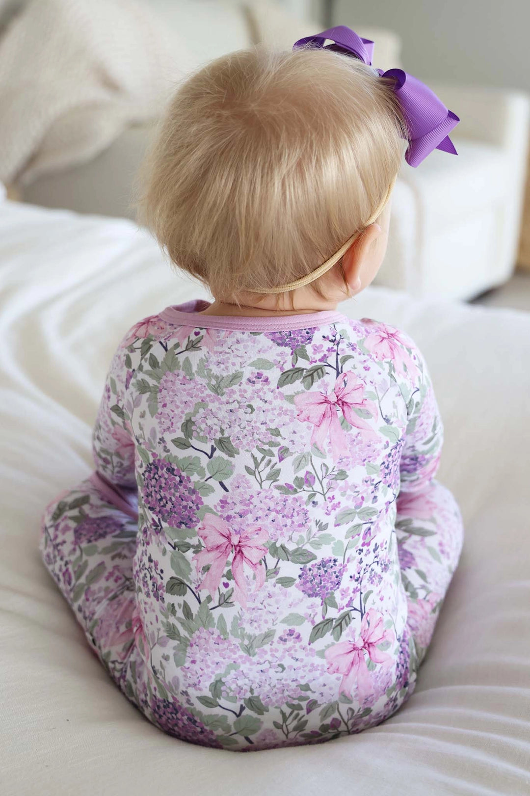 Child wearing a floral onesie sitting on a couch