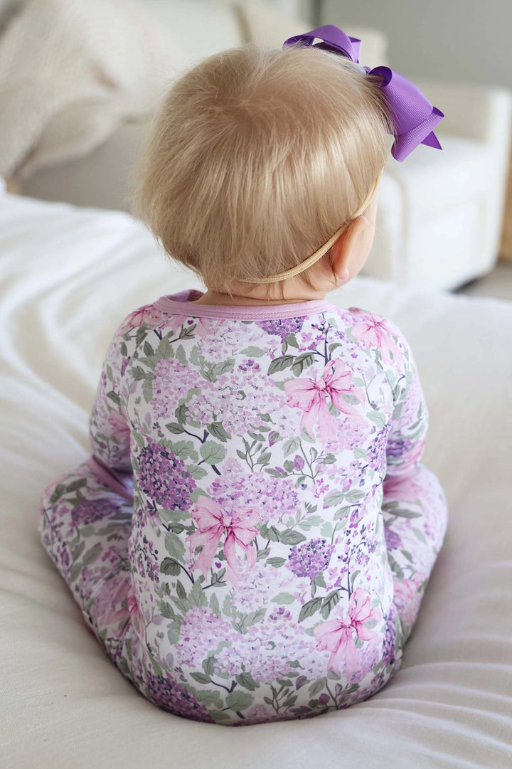 Child wearing a floral onesie sitting on a couch