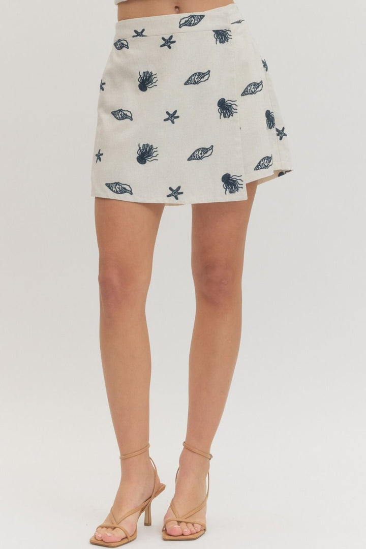 White mini skirt with blue shell pattern worn by a person on a white background