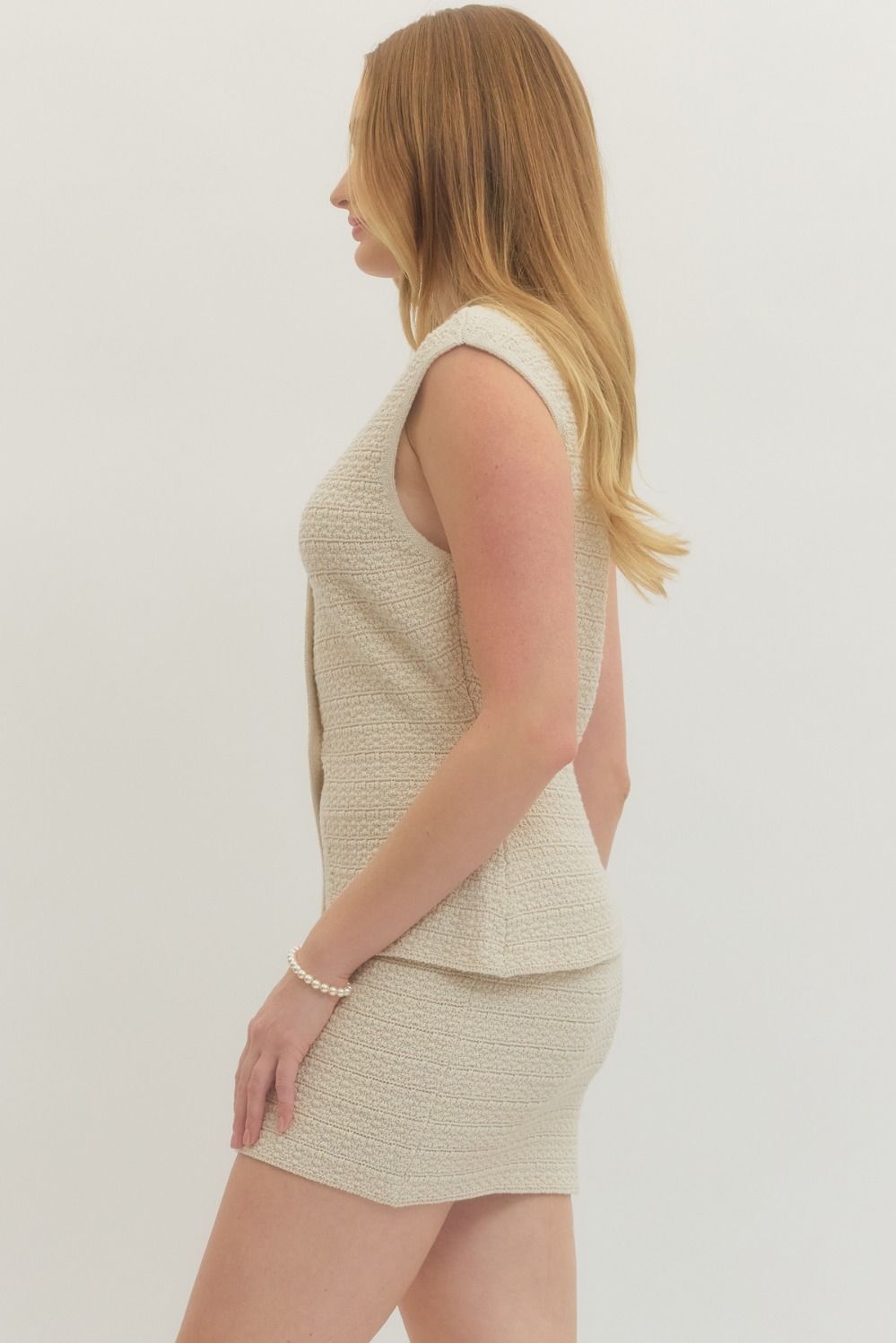 Woman wearing a beige sleeveless top and skirt set on a plain background