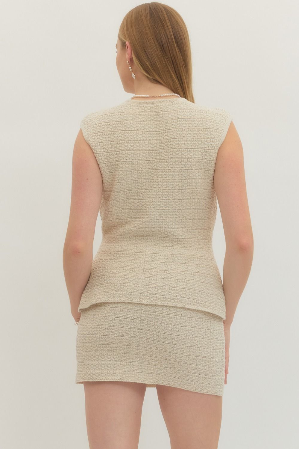 Woman wearing a beige sleeveless top and skirt set against a plain background