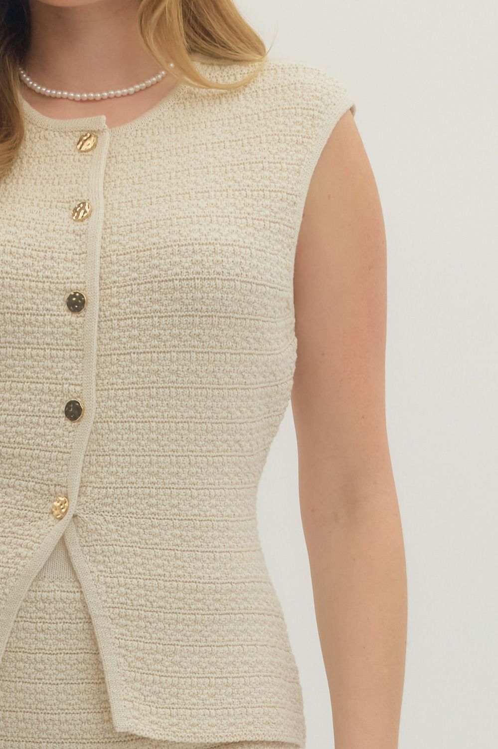 Close-up of a beige textured sleeveless top with buttons on a white background