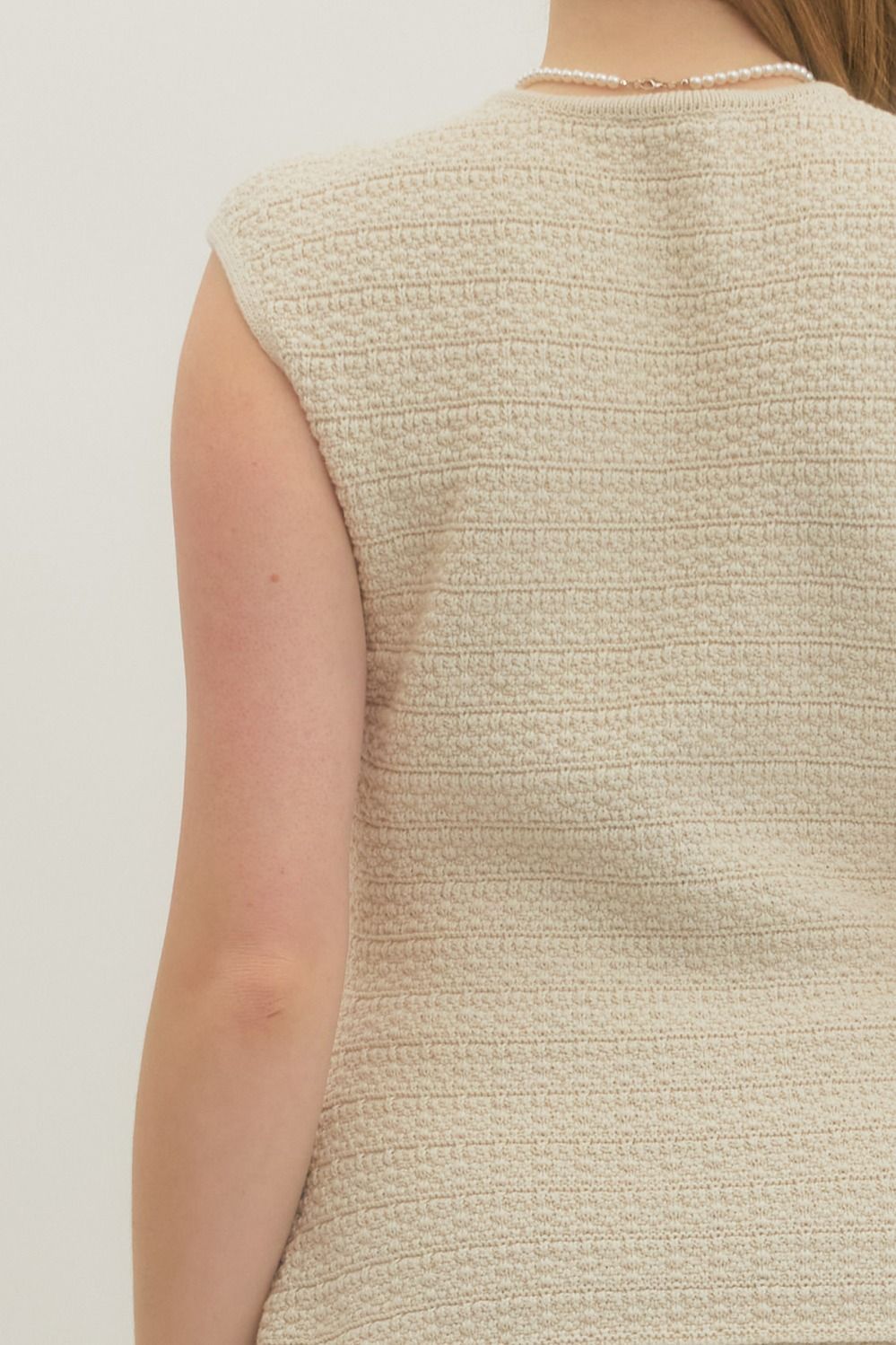 Close-up of a textured beige sleeveless top on a plain background