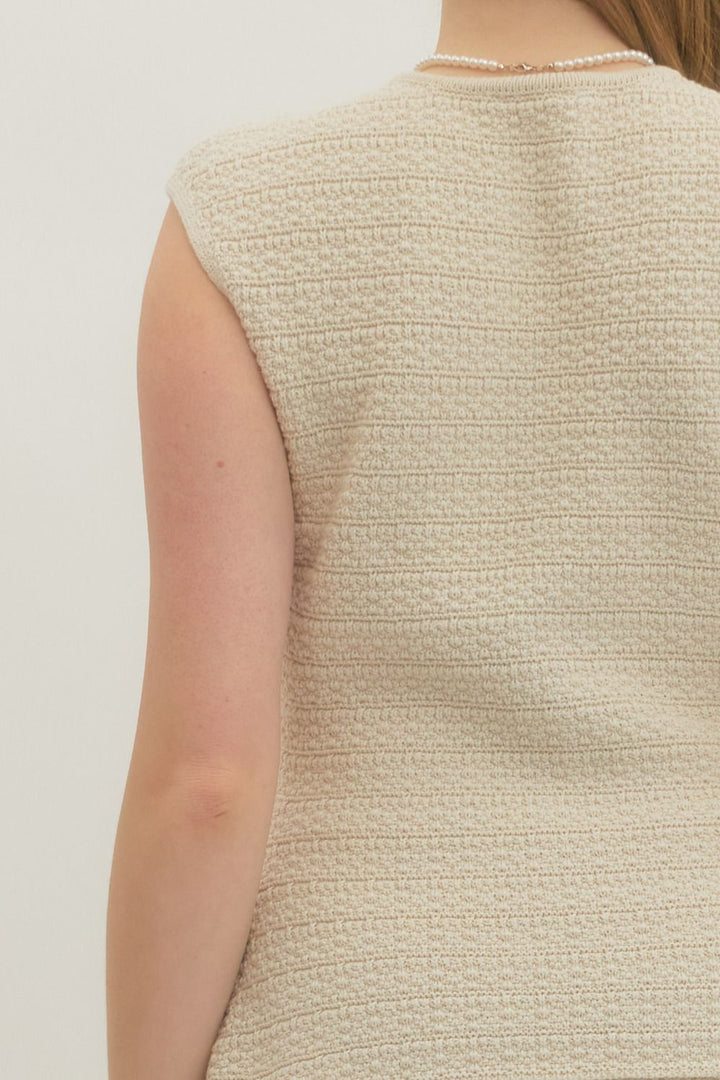 Close-up of a textured beige sleeveless top on a plain background