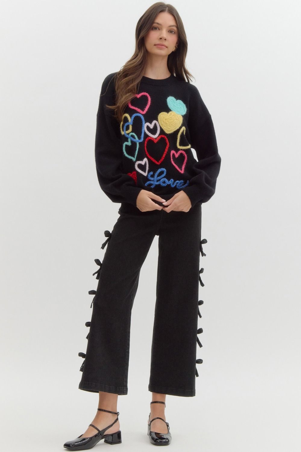 Black sweater with multicolored knit hearts on it, the word 'love' written at the bottom in blue.