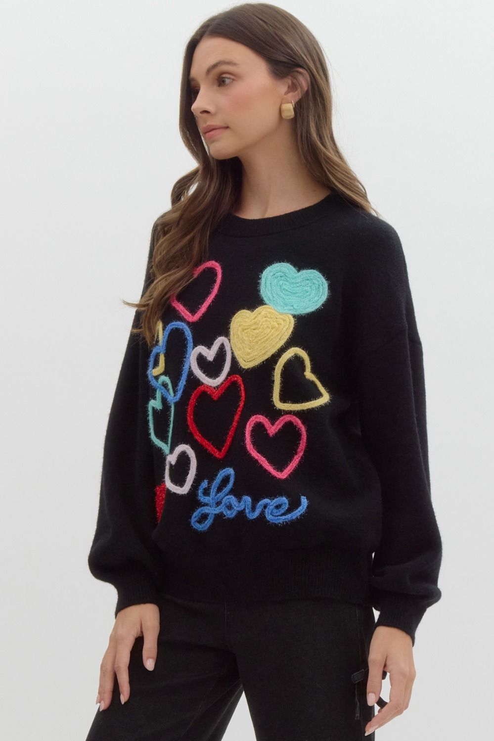 Black sweater with multicolored knit hearts on it, the word 'love' written at the bottom in blue.