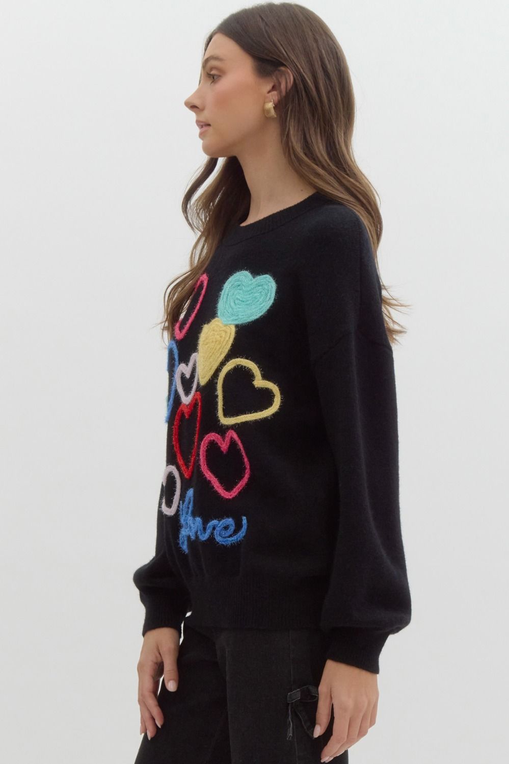 Black sweater with multicolored knit hearts on it, the word 'love' written at the bottom in blue.