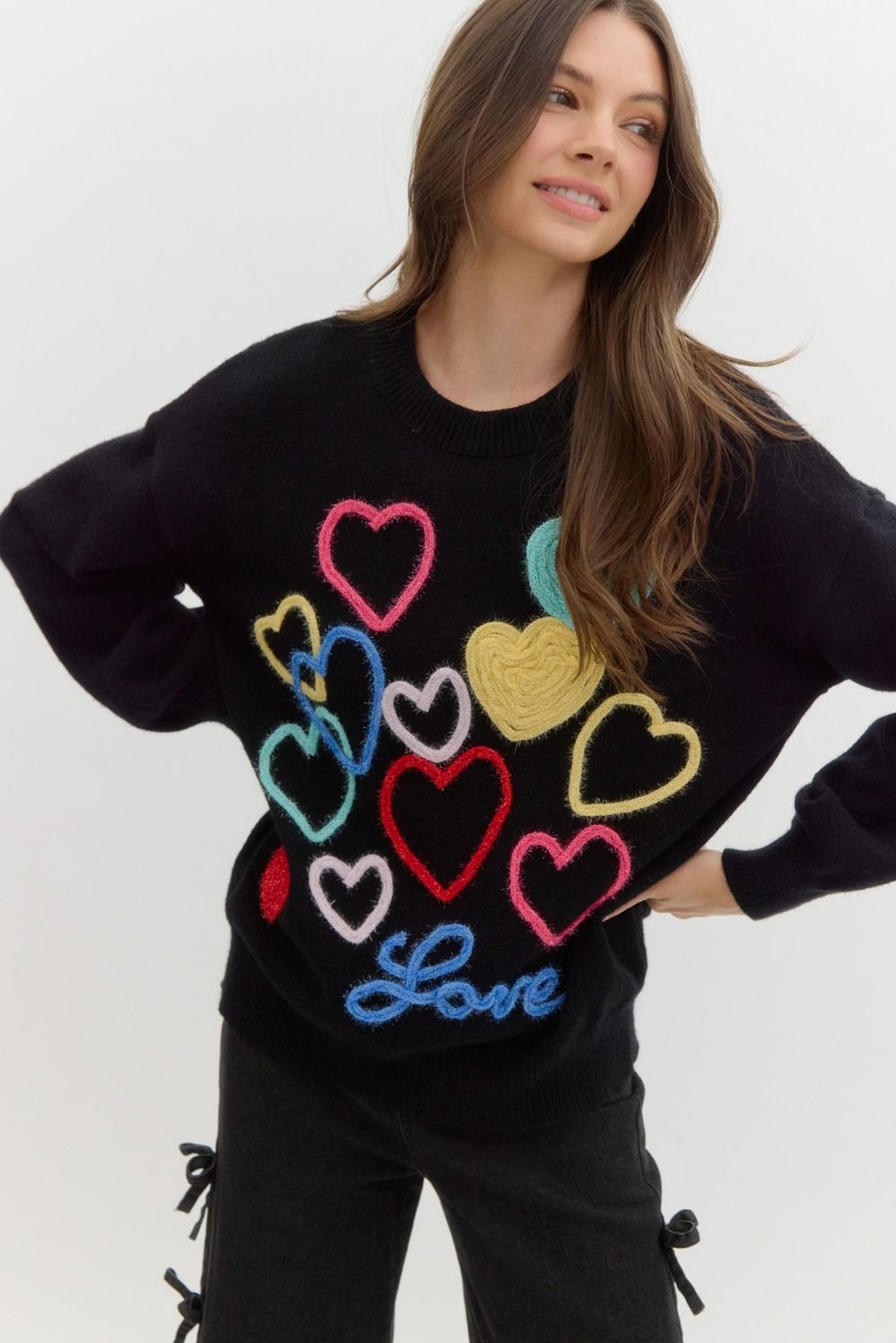 Black sweater with multicolored knit hearts on it, the word 'love' written at the bottom in blue.