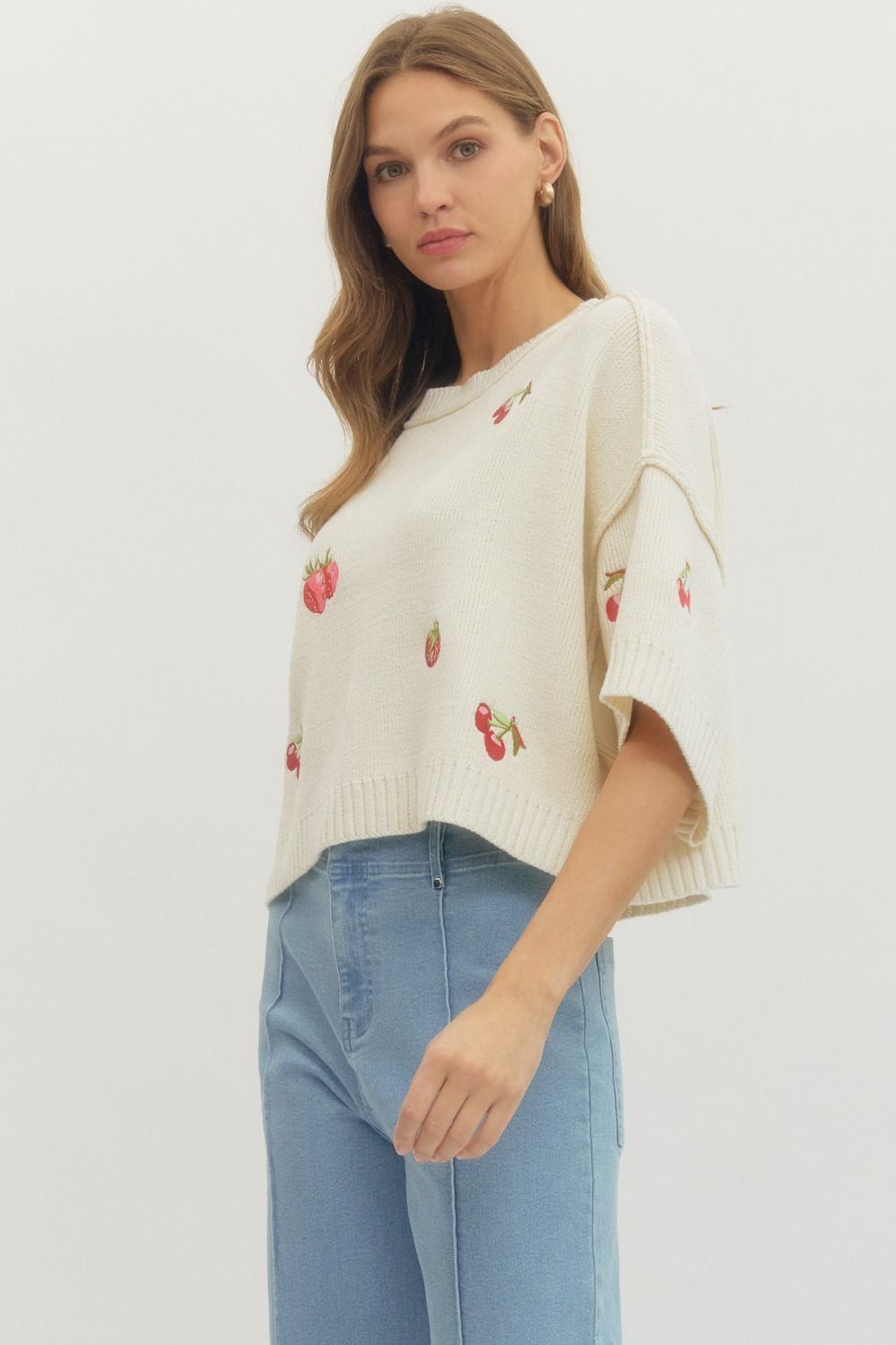 Woman wearing a beige sweater with floral patterns and blue jeans on a white background