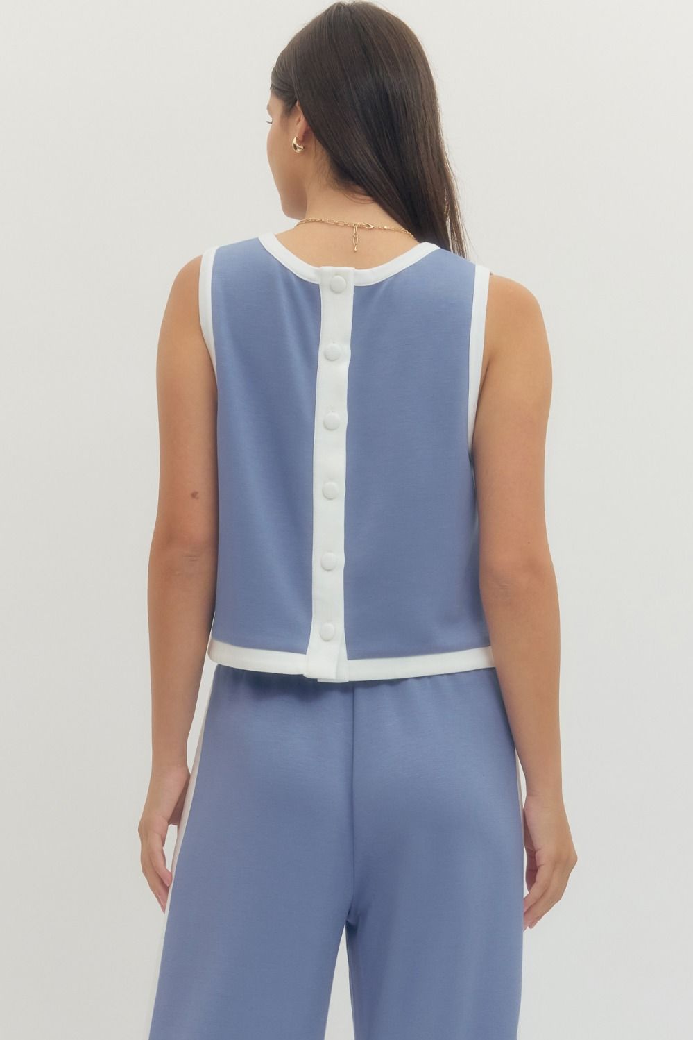 Woman wearing a blue sleeveless top with white buttons and matching pants on a light gray background
