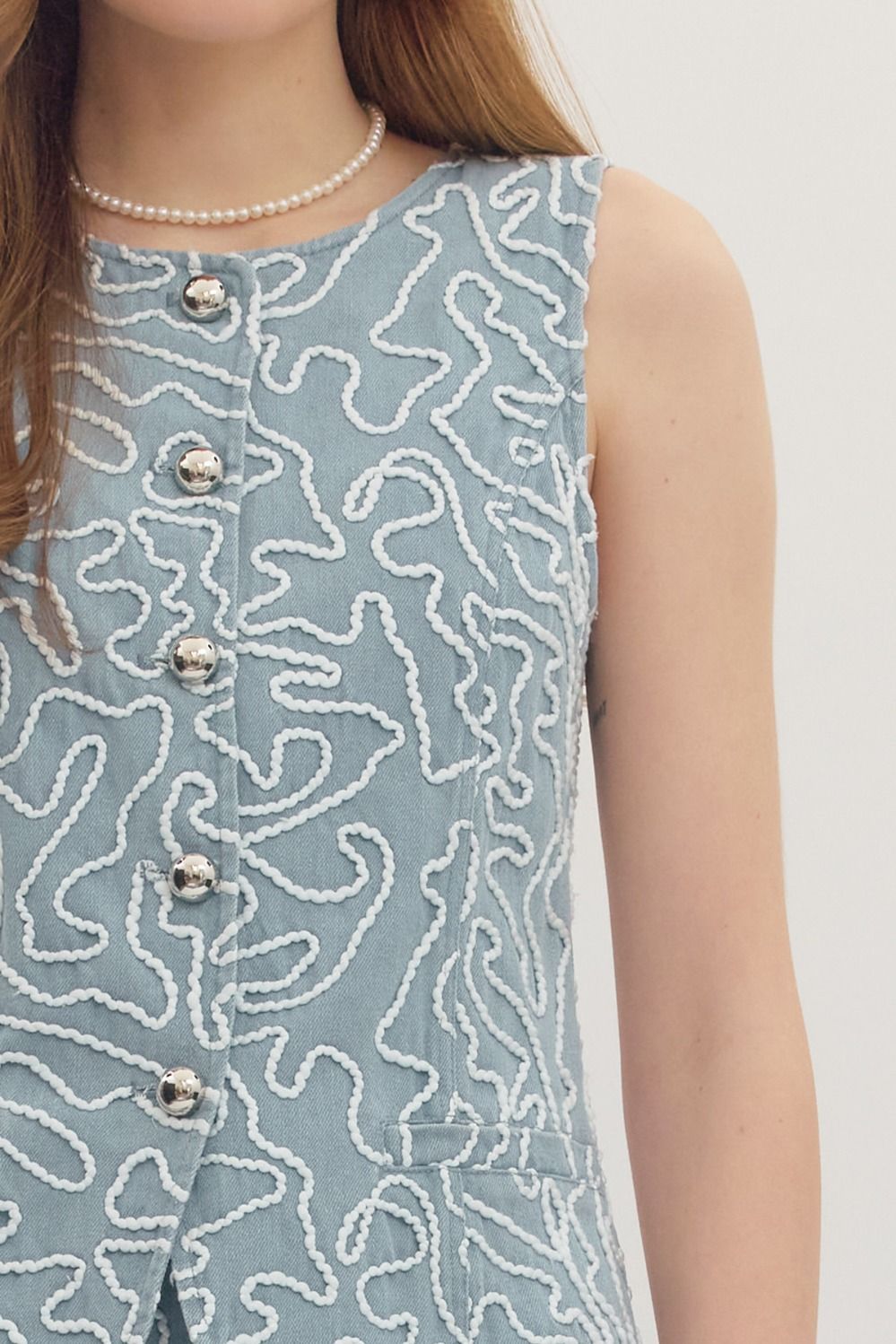Light blue sleeveless dress with white abstract pattern and silver buttons on a plain background