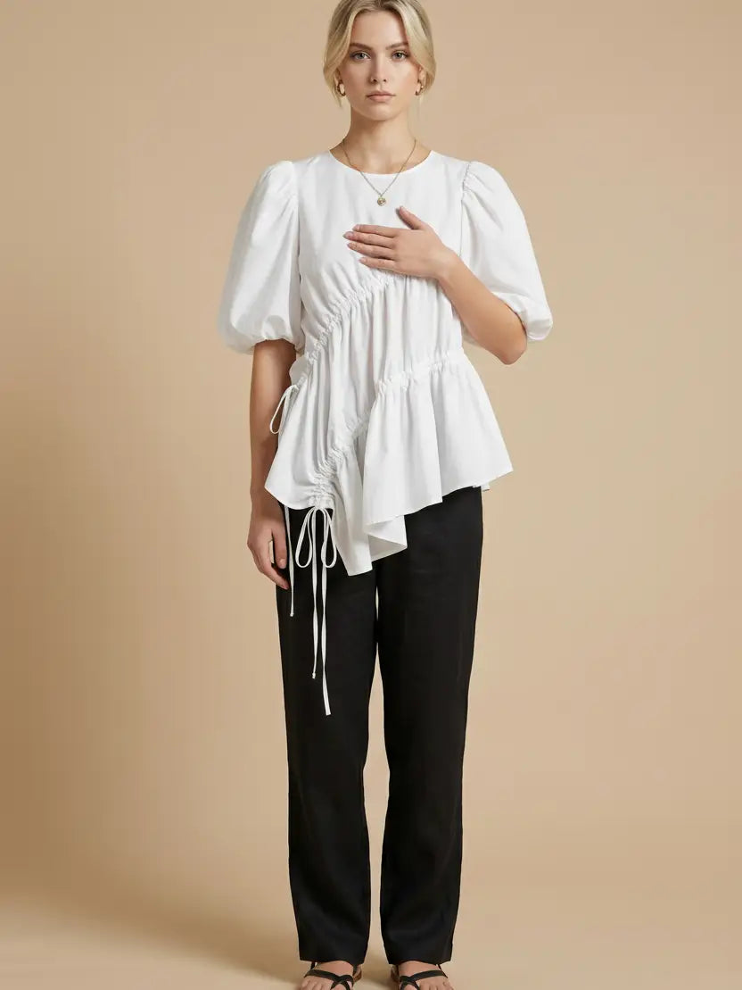 Woman wearing a white blouse with puff sleeves and black pants on a beige background