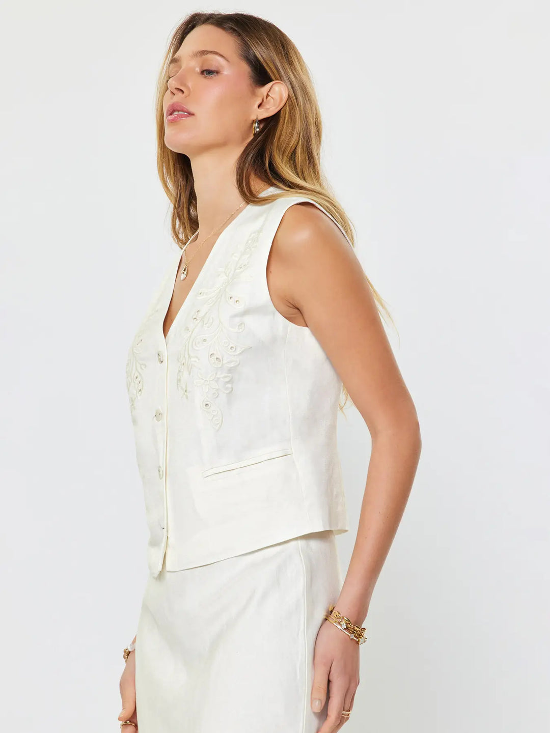 Woman wearing a white sleeveless top with floral details on a plain background