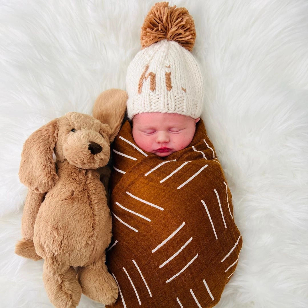 Newborn swaddled with a plush puppy wearing the natural Hi There Baby Hat