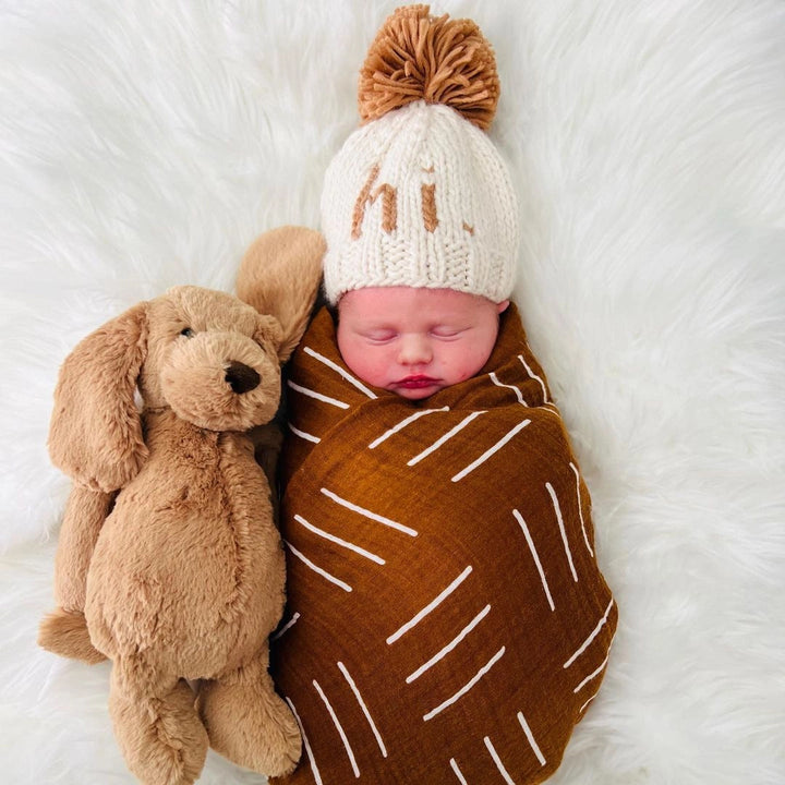 Newborn swaddled with a plush puppy wearing the natural Hi There Baby Hat