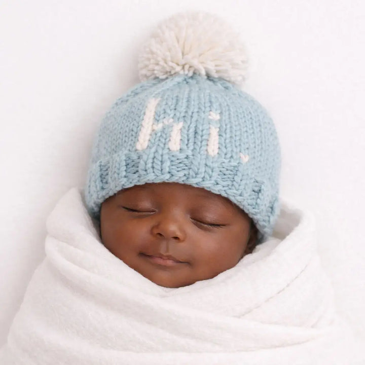 Sleeping baby swaddled in white wearing the surf blue Hi There Baby Hat