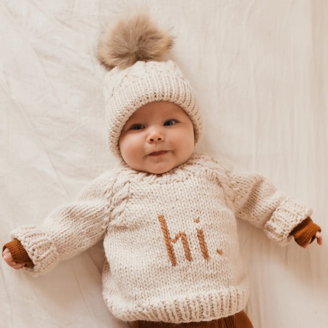 Baby lying down in the natural Hi There Baby Sweater with pecan hi. lettering