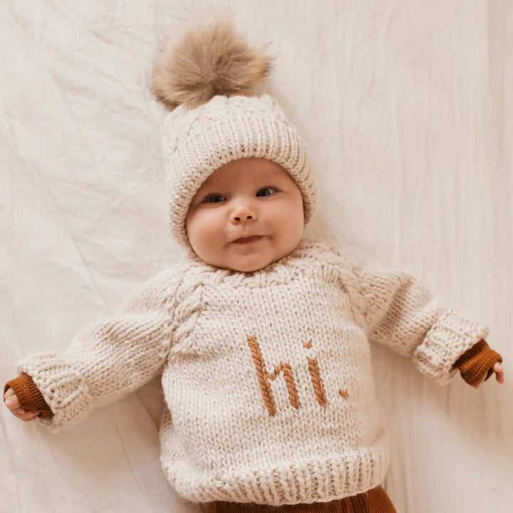Baby lying down in the natural Hi There Baby Sweater with pecan hi. lettering