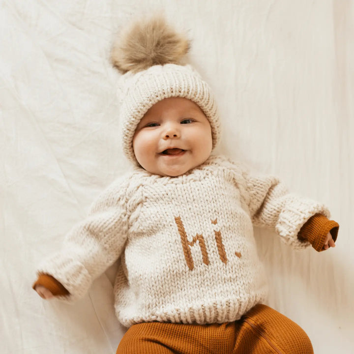 Smiling baby wearing the natural Hi There Baby Sweater with pecan hi. lettering