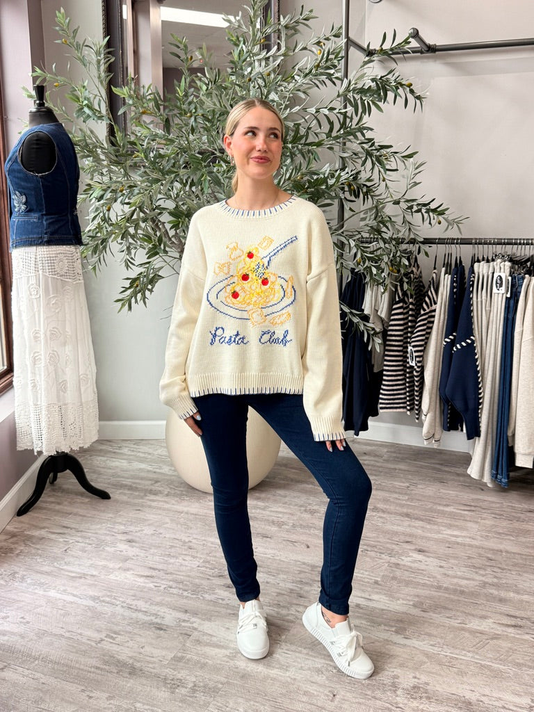 A woman modeling a cream-colored crewneck sweater with a colorful pizza graphic and the words &