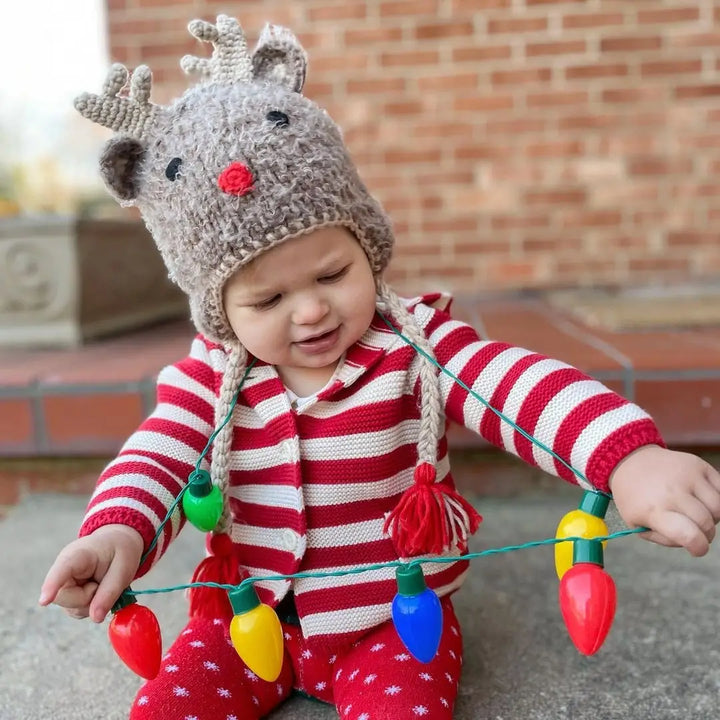 Toddler in holiday pajamas wearing the Rudolph Baby Hat while holding Christmas lights