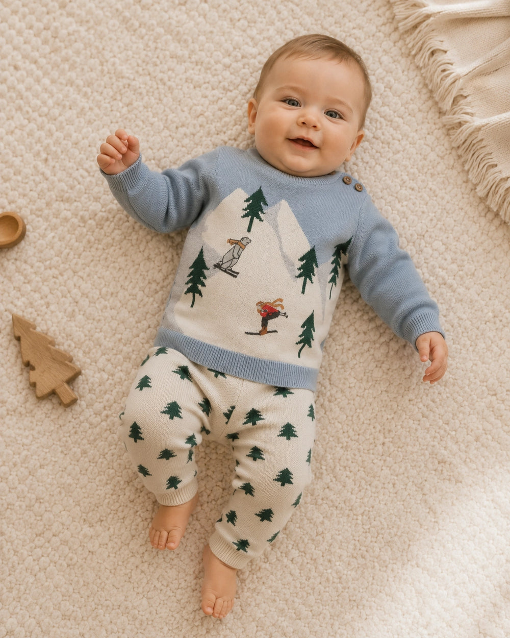 Mineral blue baby knit sweater with white mountains, evergreen trees, and skiing figures