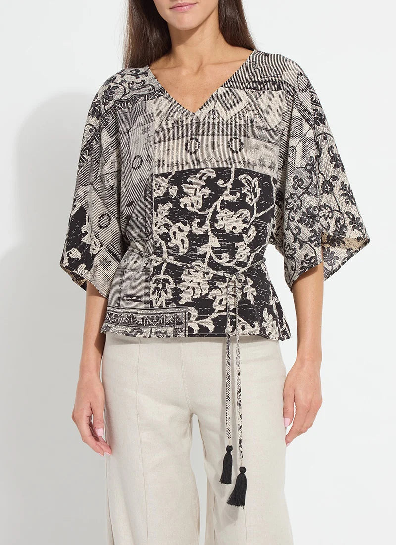 Woman wearing a patterned blouse with tassel details on a plain background
