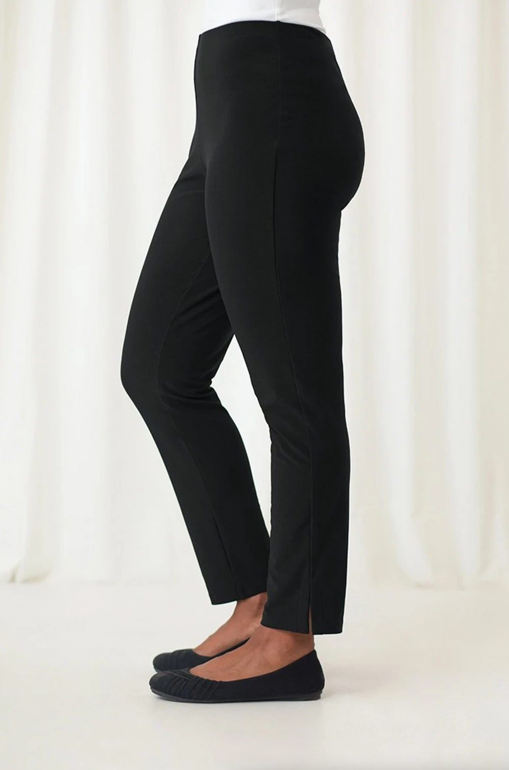 A side view of a person wearing narrow leg black pants that hit at the ankle, with a foldover waistband.